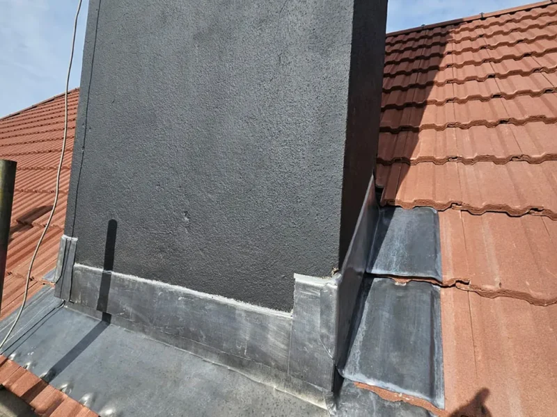 Chimney stack with a newly rendered and lead-skirted base against a red clay tile roof