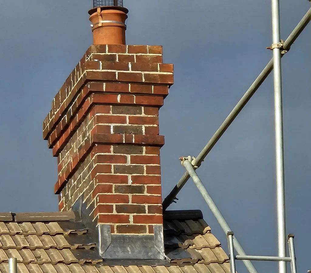 Tall rebuilt brick chimney stack with two pots against a clear blue sky
