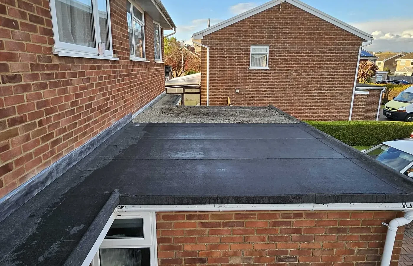 Newly completed dark flat roof over a rear extension on a red brick bungalow under blue sky
