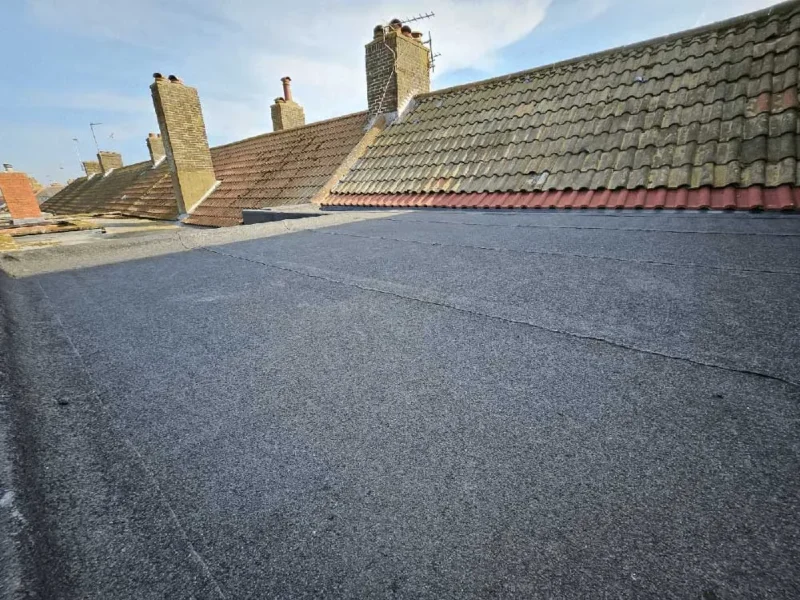 Flat roof section in the foreground with a tiled ridge and chimney stacks behind, under blue sky