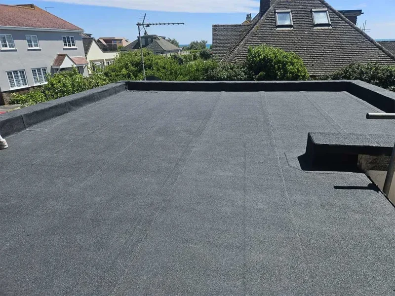 Newly completed dark grey flat roof with neat welted edges, looking out over a coastal town