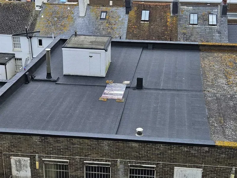 New felt flat roof with a roof-access shed, backed by an older slate roofline and chimneys