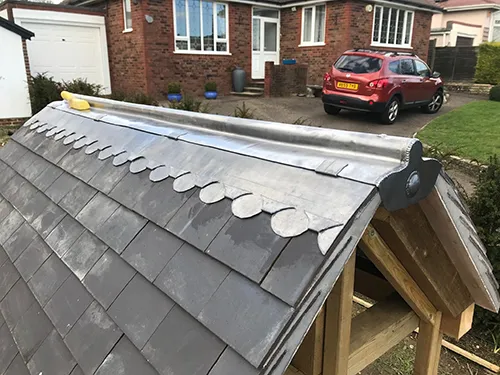 Ornamental lead roll ridge with scalloped lead detailing on a slate-covered roof structure
