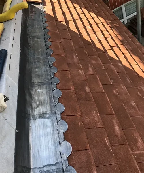 Lead valley flashing running down a red clay tile roof pitch in bright sunlight