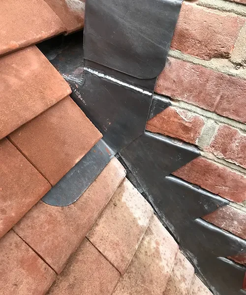 Lead step flashing dressed around a brick chimney against new clay roof tiles