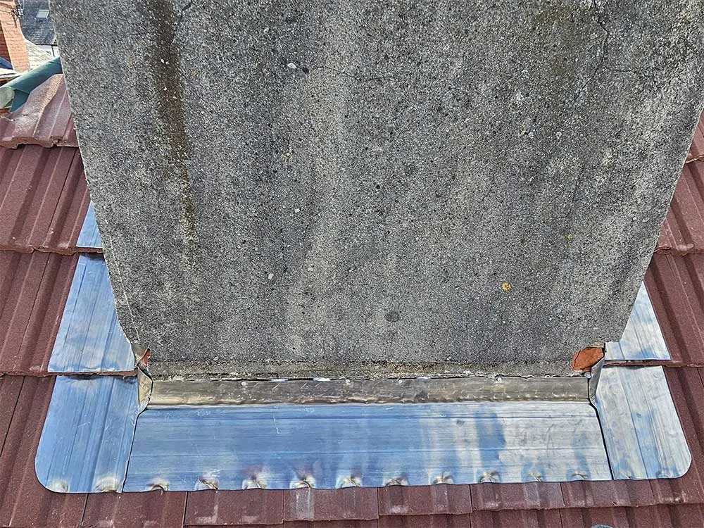 New lead soaker flashing dressed around the base of a chimney stack on a red tiled roof