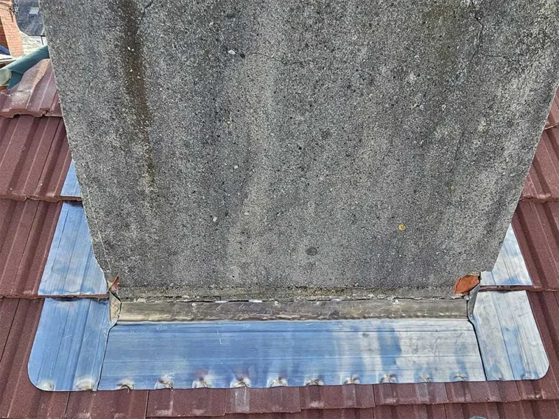 New lead soaker flashing dressed around the base of a chimney stack on a red tiled roof