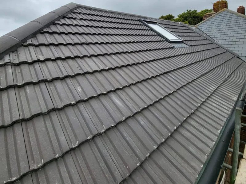 The same roof re-covered in new grey concrete interlocking tile with a clean ridge line and reset roof window flashings