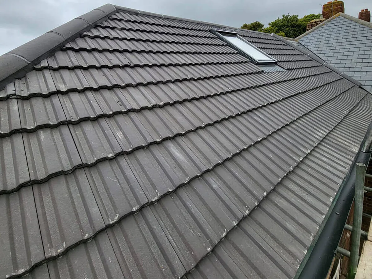The same roof re-covered in new grey concrete interlocking tile with a clean ridge line and reset roof window flashings