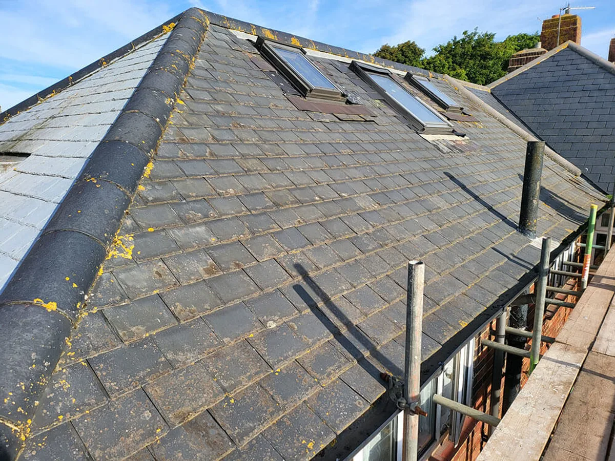 Worn slate roof heavily colonised with moss and lichen, with cracked and slipped slates around the roof windows, before stripping