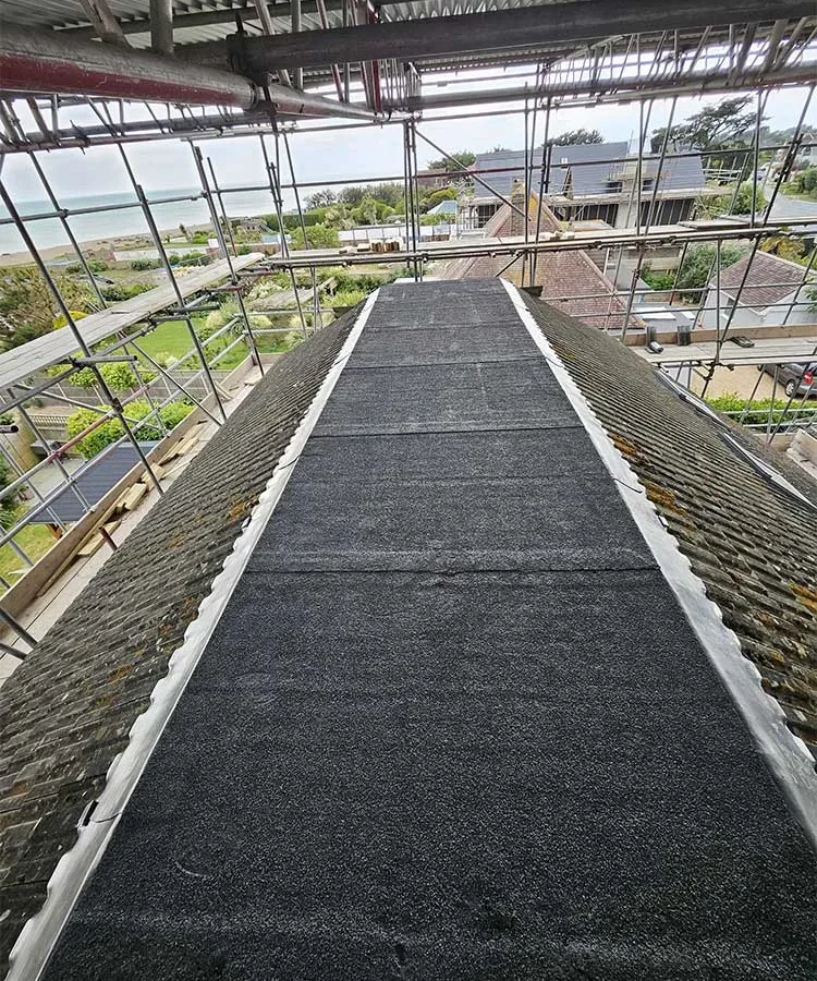 New felt valley lining laid between two aged tiled roof slopes, with a sea view beyond