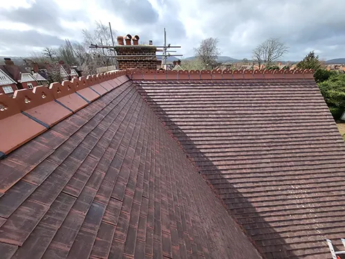 Freshly re-tiled hip roof ridge with the chimney stack and scaffold in place, rooftops and downland beyond