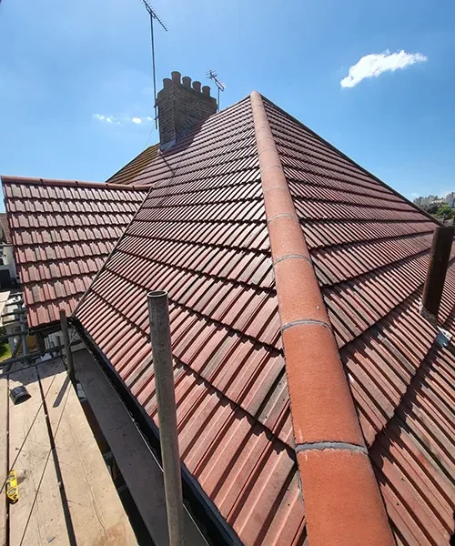 Converging hip lines on a red clay tile roof with a chimney stack against a clear blue sky