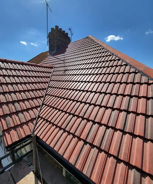 New red clay tile roof laid in neat diagonal courses up to the ridge and chimney stack