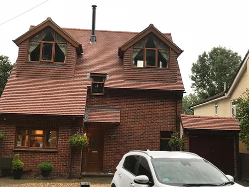 Completed re-roof in red concrete tile on a detached house with twin dormers and a rebuilt chimney