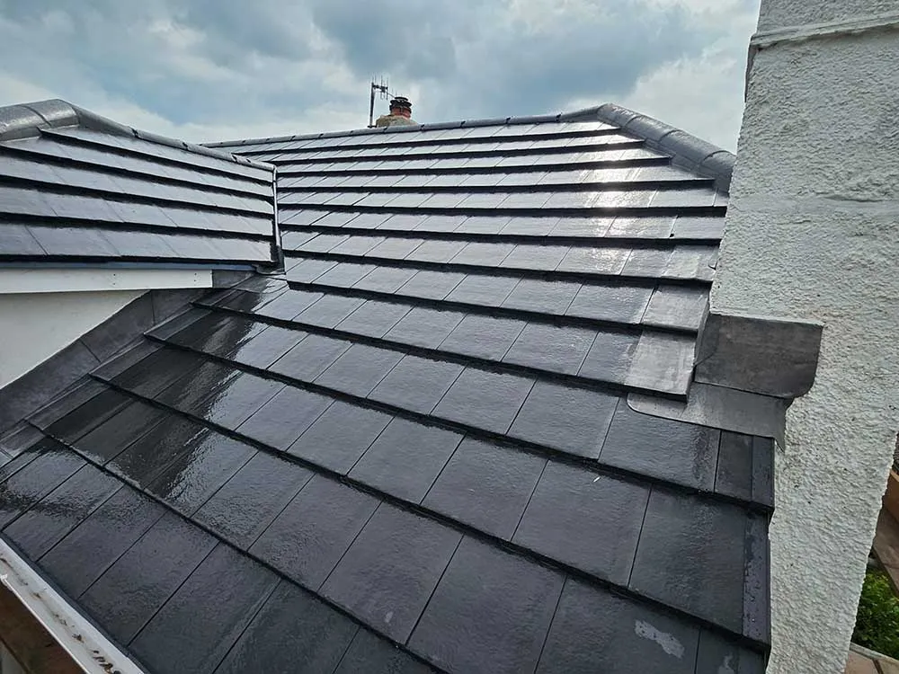 New grey concrete interlocking tile roof with hip detail and chimney, tiles glistening after rain