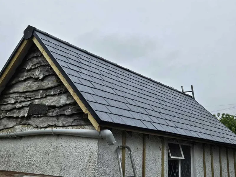 New dark grey slate-effect tiled roof on a gable end, viewed against a soft blue sky